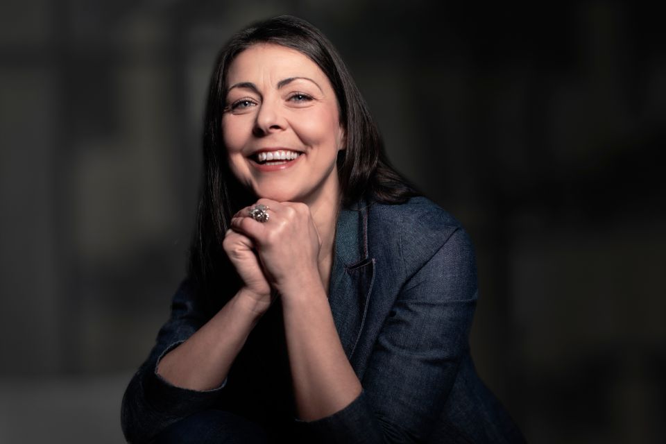 woman sitting at a table smiling to camera in a dark room